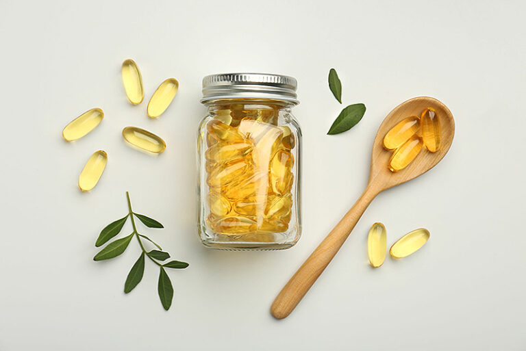Bottle, vitamin capsules, spoon and leaves on white background, flat lay.