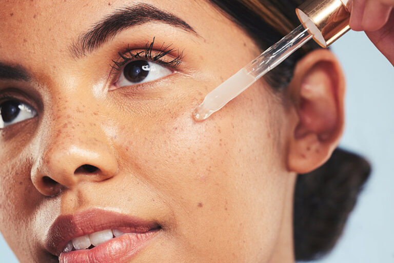 Woman, face oil and serum in studio for beauty of aesthetic skincare, dermatology and makeup on blue background. Closeup of model with dropper for facial cosmetics, hyaluronic acid and clean shine.